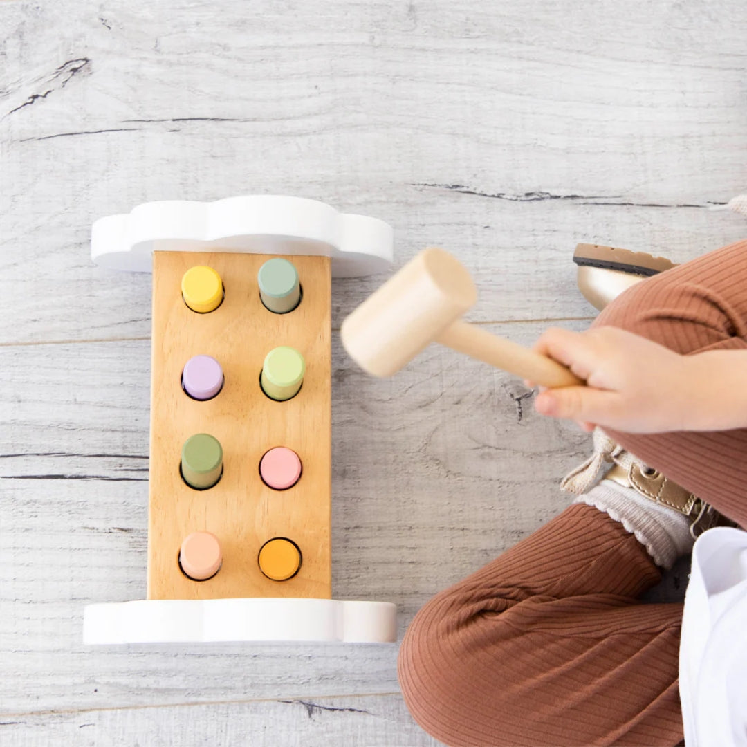 Child playing with a Pearhead wooden hammer and colorful pegs on a light wooden surface