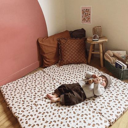 Child lying on a leopard print mat in a cozy room with pillows and a small table.