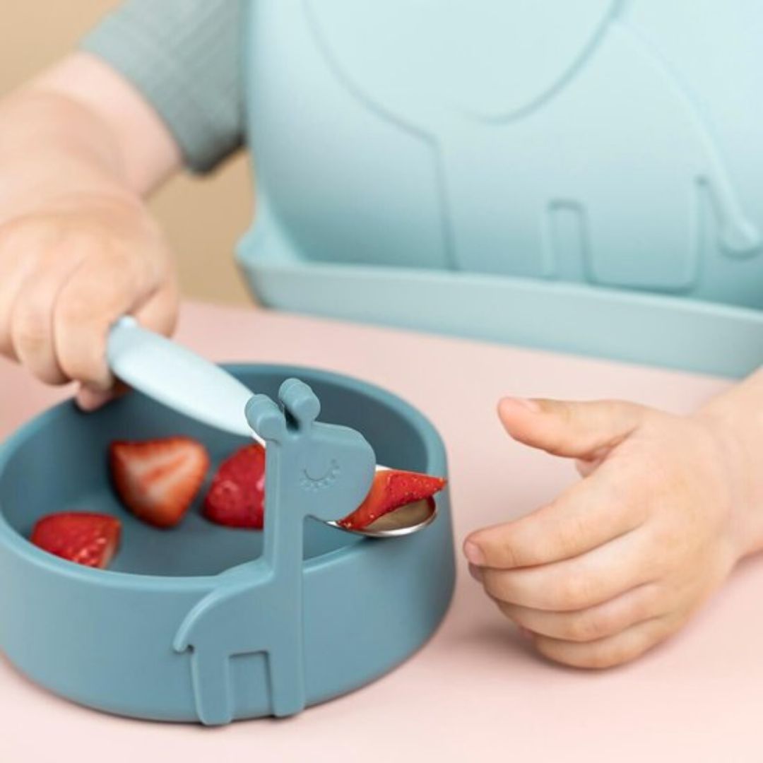 Child using a blue giraffe-shaped bowl and spoon to eat strawberries.