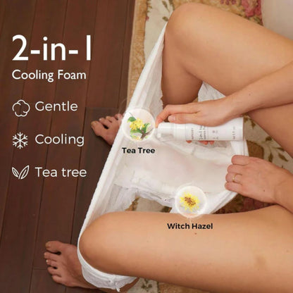 Person holding a 2-in-1 cooling foam with tea tree and witch hazel ingredients, sitting on a wooden floor.