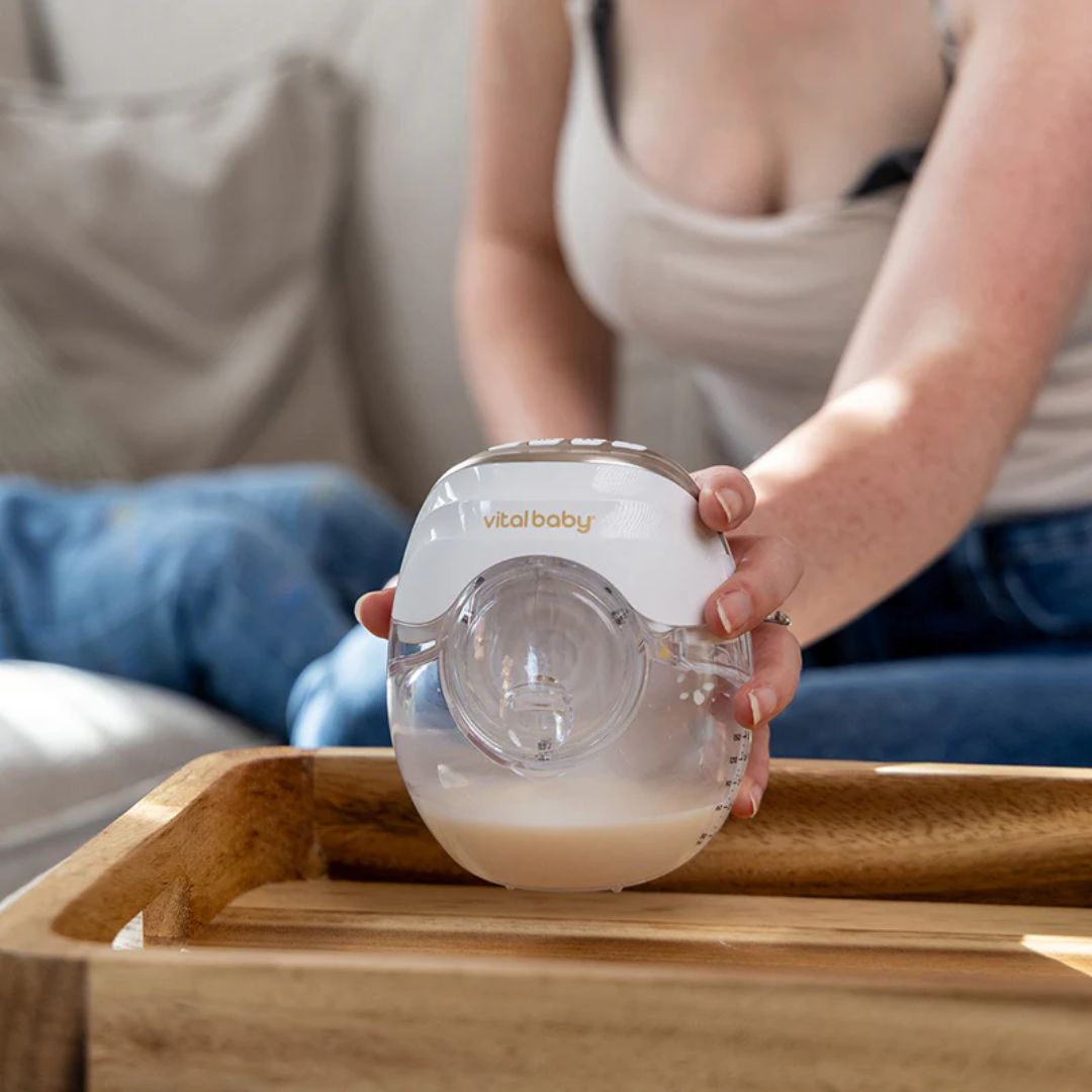 Person holding a baby bottle with 'vitalbaby' branding on a wooden tray.