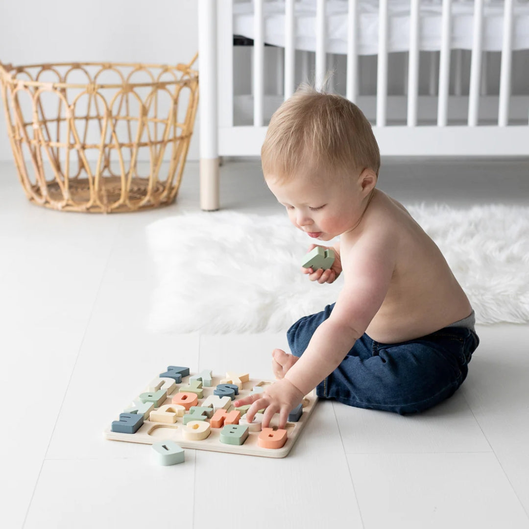 Child playing with a Pearhead wooden puzzle on a white floor.