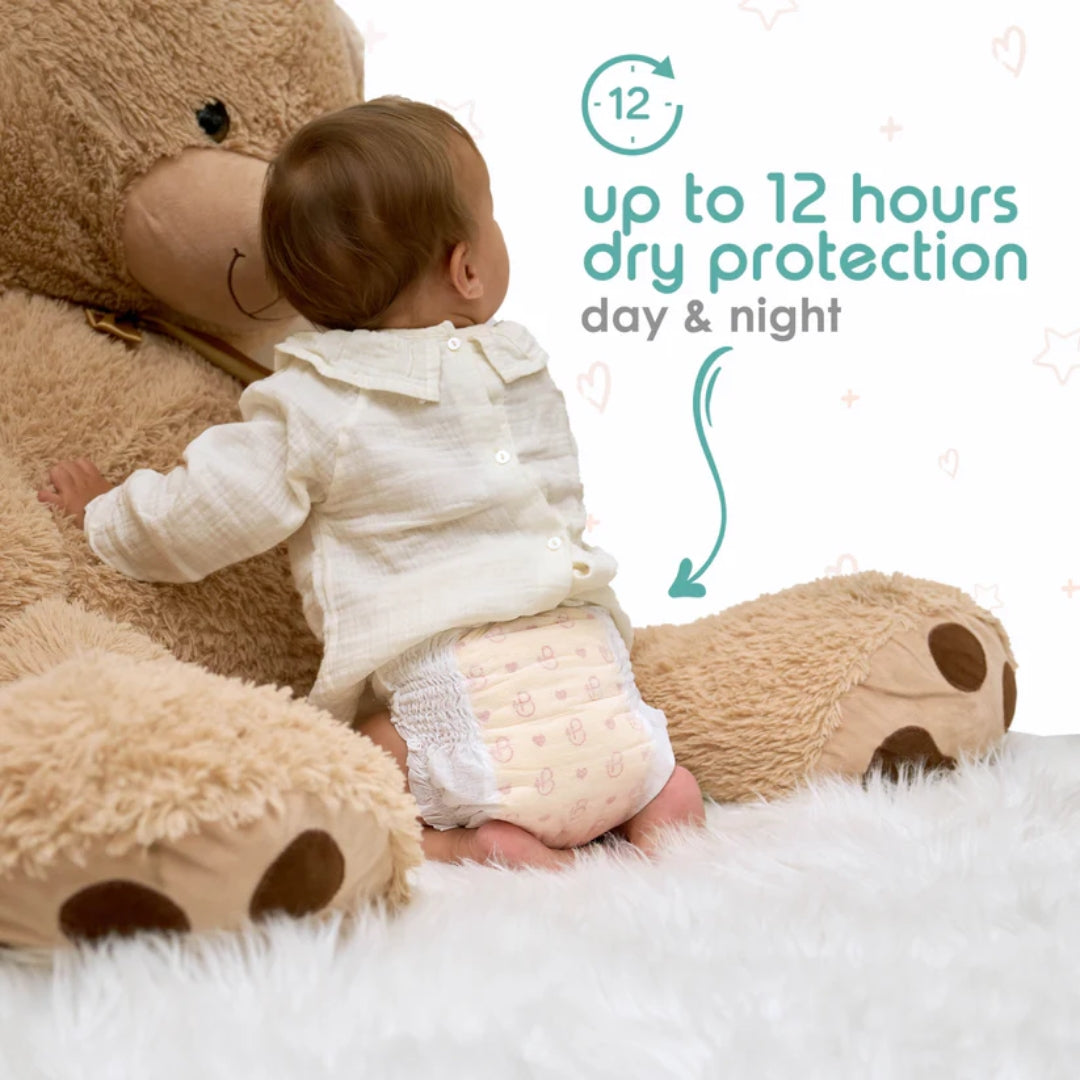 Baby in a diaper hugging a teddy bear with text about dry protection, on a white background.