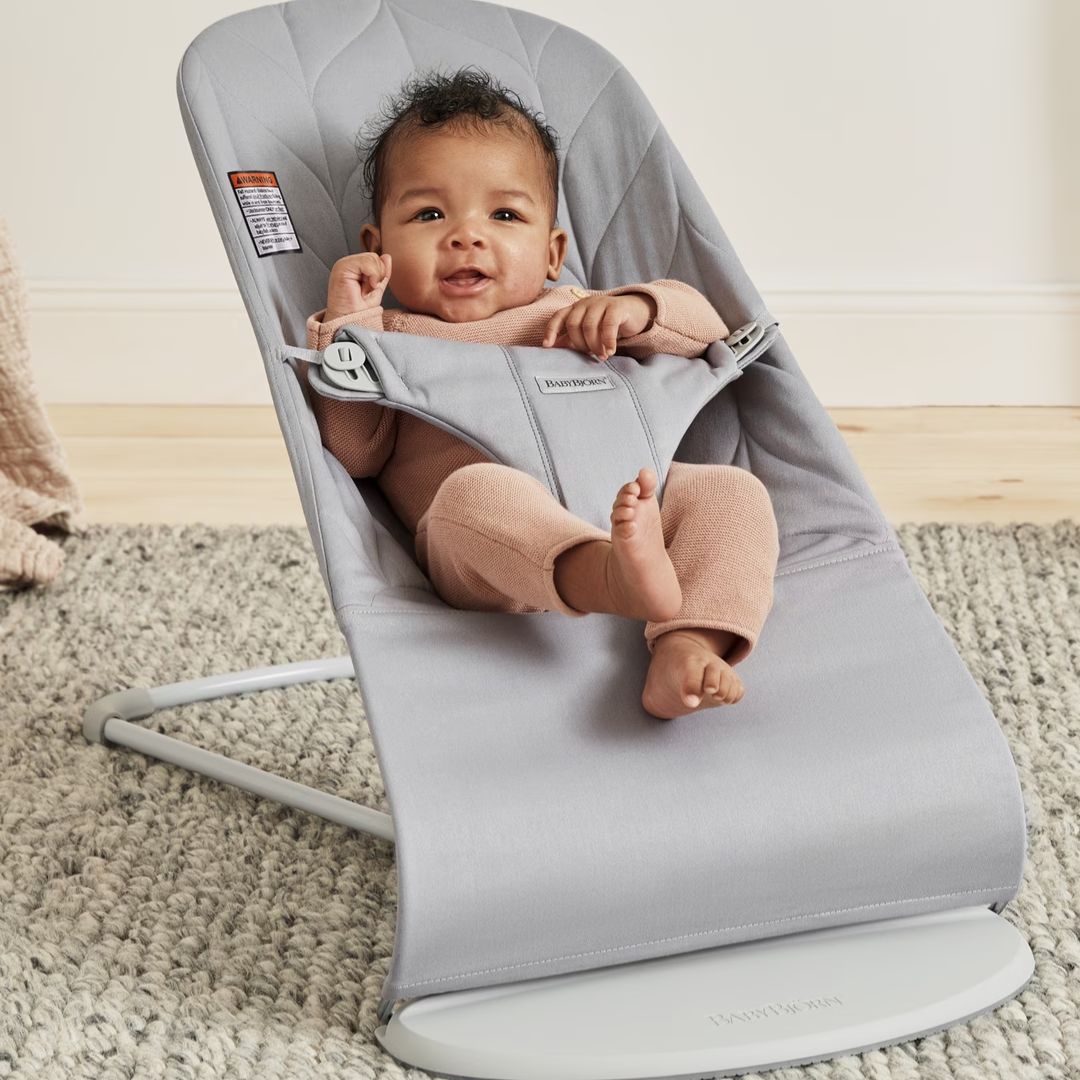 Baby in a gray BabyBjorn baby bouncer on a carpeted floor