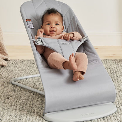 Baby in a gray BabyBjorn baby bouncer on a carpeted floor