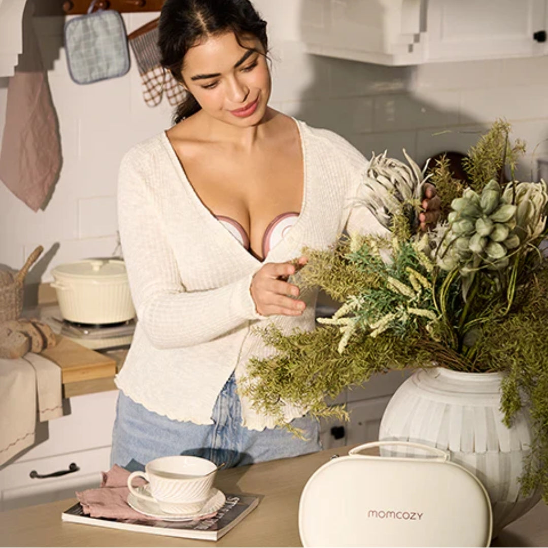 Woman in a kitchen holding a plant, with a 'momcozy' breast pump on the counter.