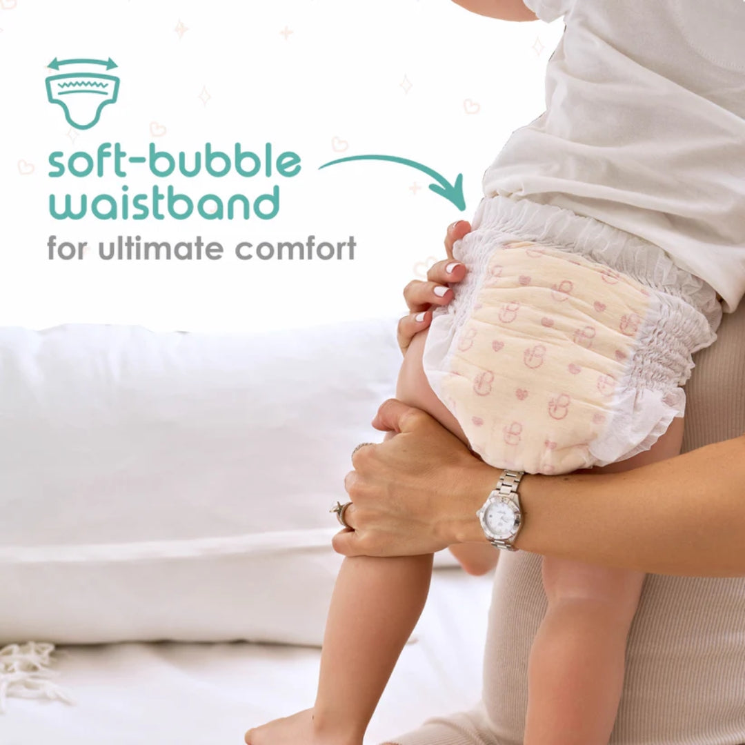 Baby wearing a diaper with a soft-bubble waistband, held by an adult, on a light background.